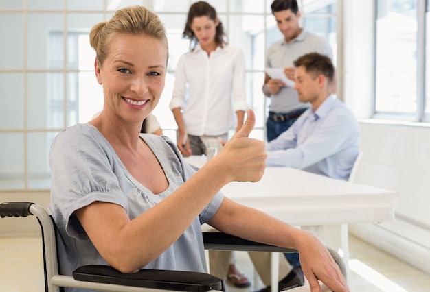 Casual femme d&#39;affaires en fauteuil roulant, souriant à la caméra avec l&#39;équipe derrière elle