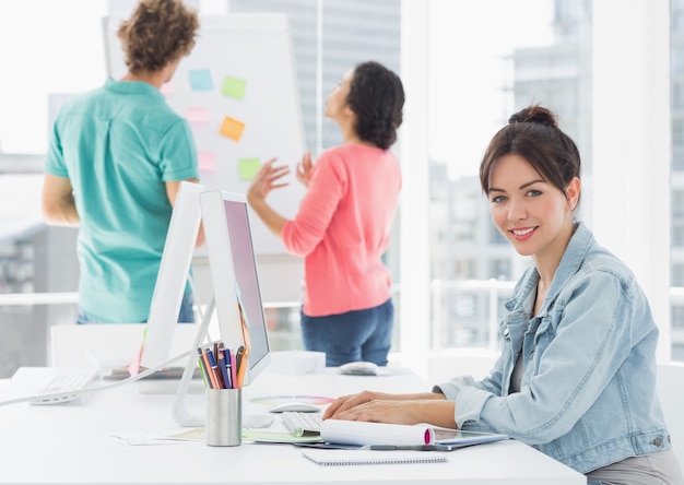 Casual femme à l&#39;aide d&#39;ordinateur avec des collègues derrière au bureau