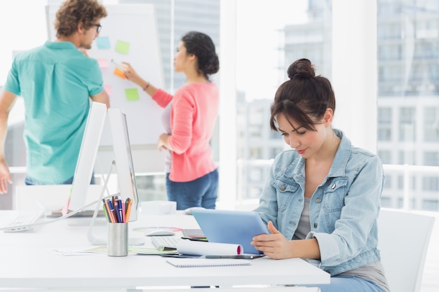 Casual femme à l&#39;aide de tablette numérique avec des collègues derrière au bureau