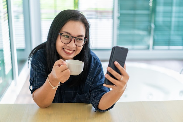 Casual femme asiatique heureuse boire du café et regarder smartphone