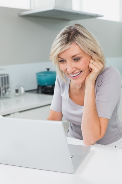 Casual femme heureuse en utilisant un ordinateur portable dans la cuisine