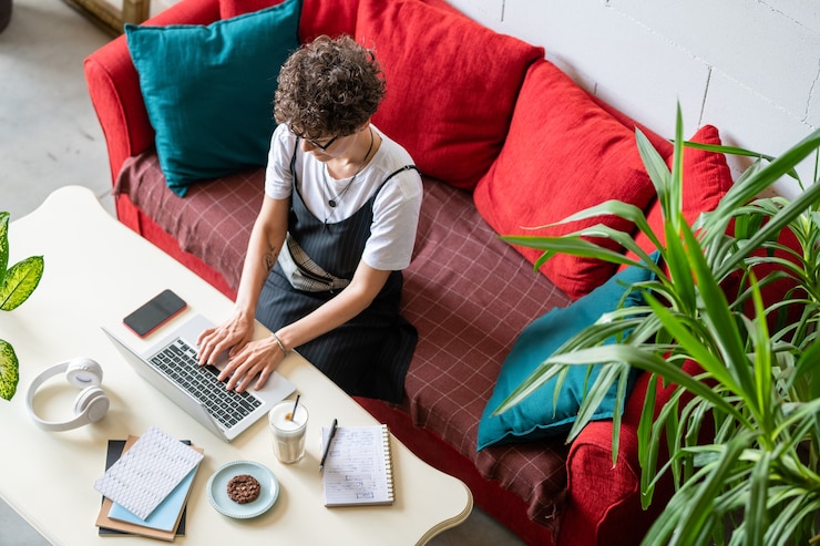 Photo casual jeune femme assise sur un canapé devant un ordinateur portable, taper et surfer sur le net tout en travaillant à distance