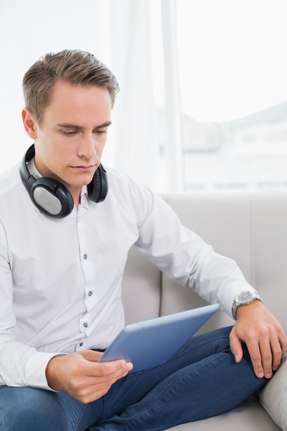 Casual jeune homme sérieux à l&#39;aide de tablette numérique sur canapé