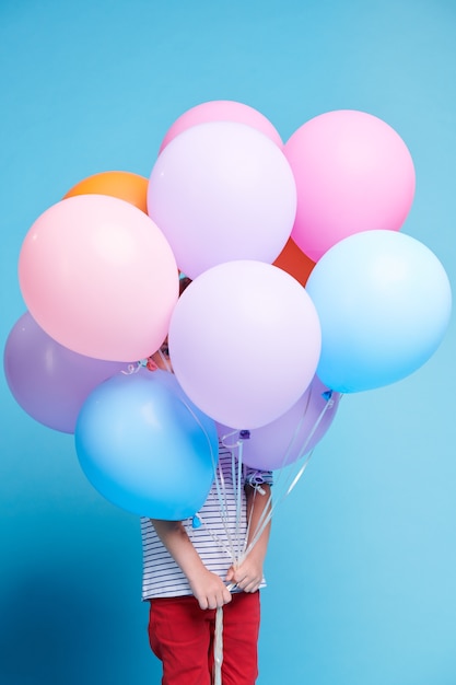 Casual petite fille furtivement à travers un petit trou entre les ballons colorés tout en tenant un tas d'entre eux devant son visage