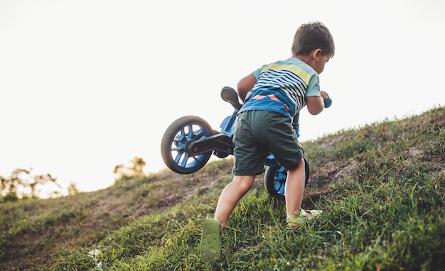 Caucasian boy porte le vélo sur une colline tout en jouant dans un champ au cours d'une soirée d'été