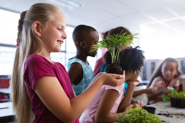 Caucasian girl smiling tout en tenant un semis de plantes dans la classe à l'école