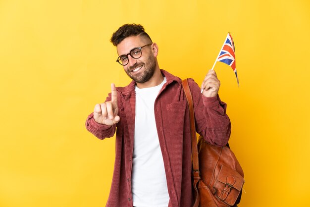 Caucasian man holding un drapeau du Royaume-Uni isolé sur fond jaune montrant et en soulevant un doigt