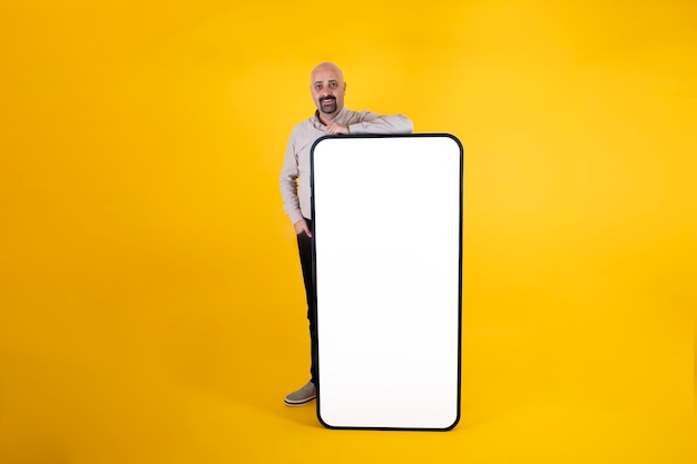 Caucasian man standing by big cell phone mock up pointant vers l'écran blanc vierge de smartphone