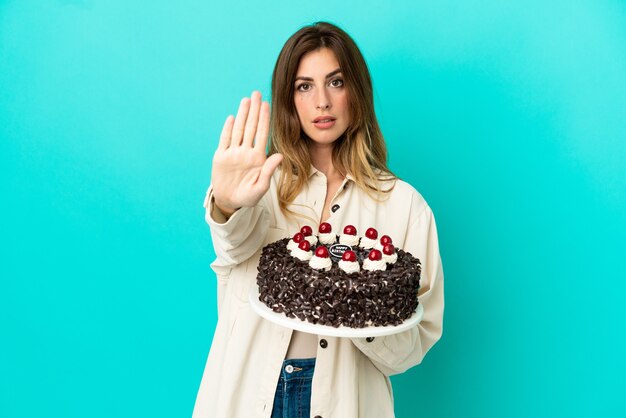 Caucasian woman holding birthday cake isolé sur fond bleu faisant un geste d'arrêt