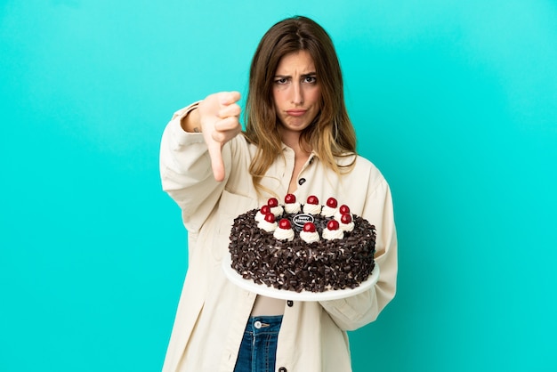 Caucasian woman holding birthday cake isolé sur fond bleu montrant le pouce vers le bas avec une expression négative