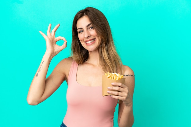 Caucasian woman holding fried chips isolé sur fond bleu montrant signe ok avec les doigts