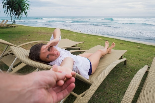 Caucasian woman in chair près de la plage tenant la main de son mari Suivez-moi concept