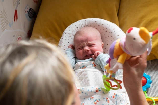 Caucasien bébé de deux mois sur le lit à la recherche d'un pouf jouet pleurer. Émotion négative de l'enfant