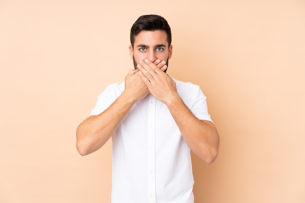 Caucasien bel homme isolé sur un mur beige couvrant la bouche avec les mains