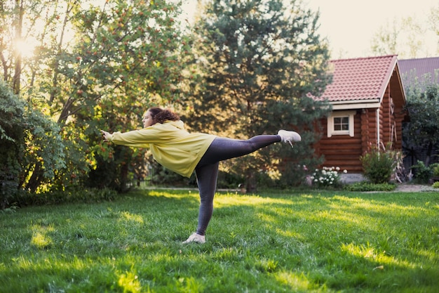 Photo caucasien grosse femme debout sur une main faisant du yoga à l'extérieur portant des vêtements de sport sur l'herbe verte sur