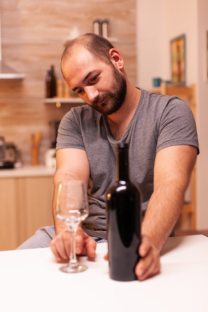 Caucasien Solitaire Dans Le Désespoir Tenant Et Regardant Une Bouteille De Vin. Maladie De La Personne Malheureuse Et Anxiété Se Sentant épuisée Par Des Problèmes D'alcoolisme.