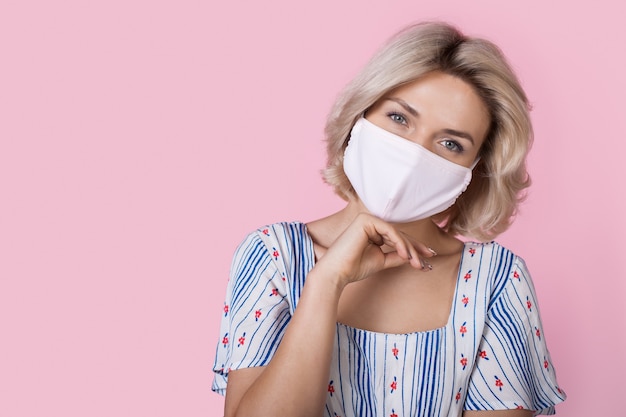 Caucasienne femme aux cheveux blonds portant une robe d'été sourit à la caméra avec un masque médical