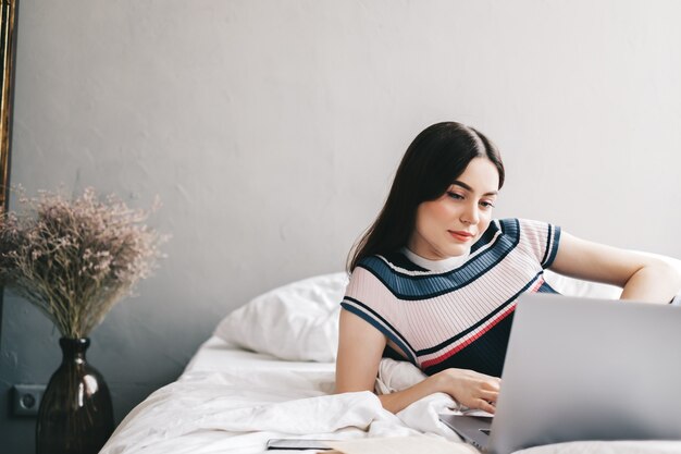 Caucasienne femme reposant sur un lit à la maison et utilisant un ordinateur portable.