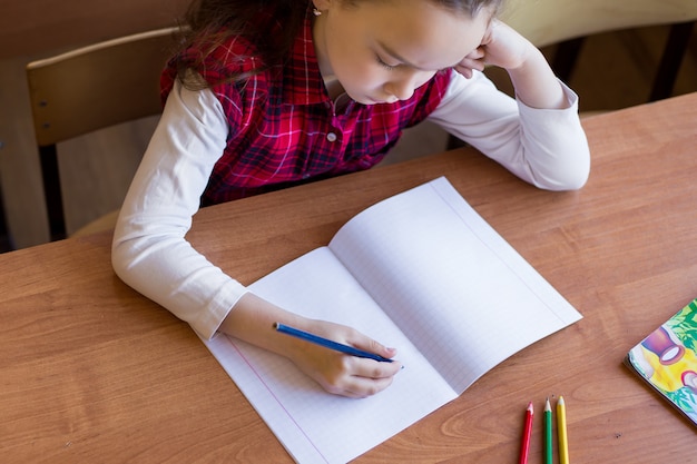 Caucasienne fille assise au bureau dans la salle de classe et commence à dessiner dans un cahier pur.