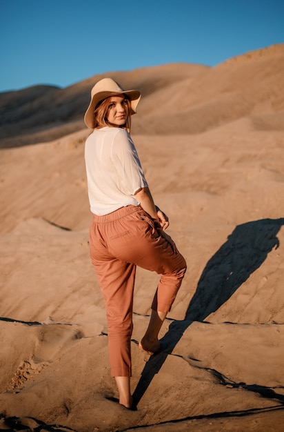 Caucasienne jeune belle fille seule est dans un chaud. Coucher de soleil dans le désert. Fille marchant sur le sable doré.