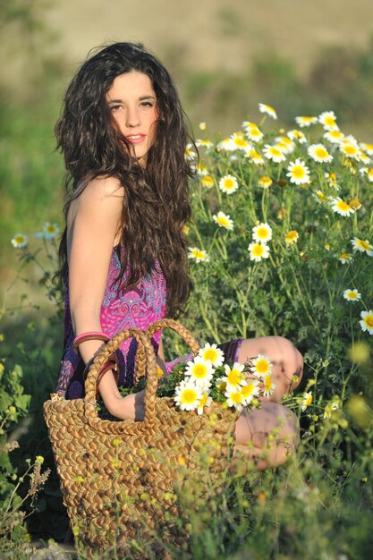 Caucasienne jeune femme en robe à motifs violets et sac à main assis dans le champ cueillir des fleurs