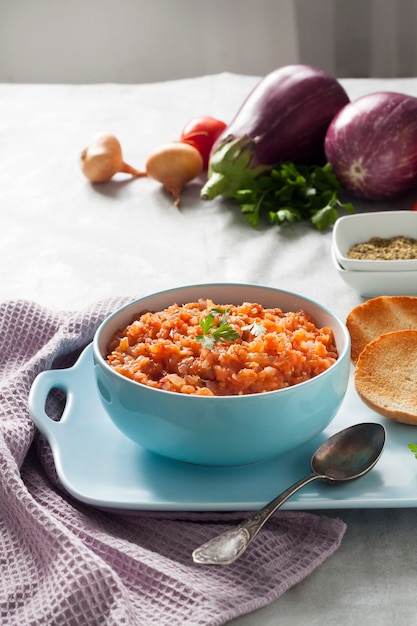 Caviar d'aubergine dans un bol bleu et légumes frais sur fond.