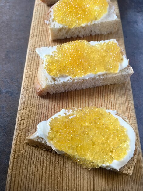 Caviar de brochet sur des sandwichs, des morceaux de pain blanc et du beurre sur une planche de bois.