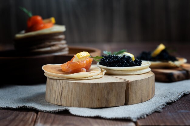 Photo caviar d'esturgeon noir et morceaux de saumon sur des crêpes sur une assiette en bois en gros plan