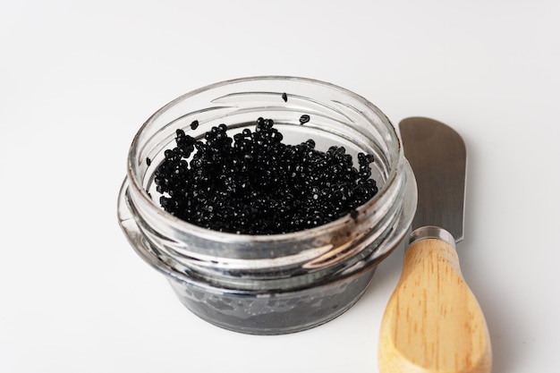 Caviar noir dans un bocal en verre et spatule sur verre blanc