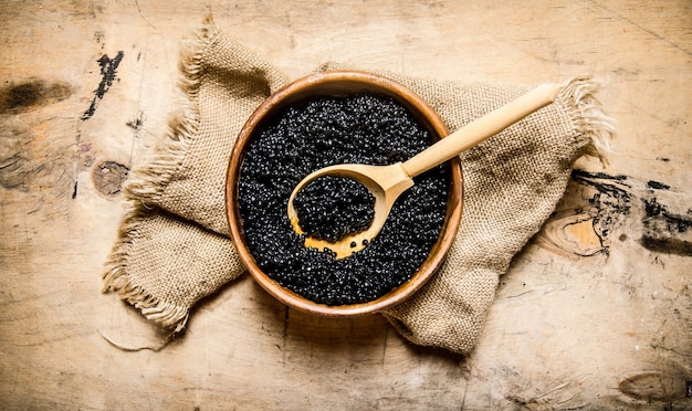 Caviar noir dans un bol en bois sur tissu ancien. Sur une table en bois. Vue de dessus