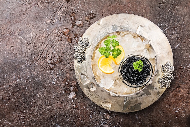 Caviar noir dans un bol en verre sur de la glace avec du citron gros plan sur la vue de dessus de la surface sombre