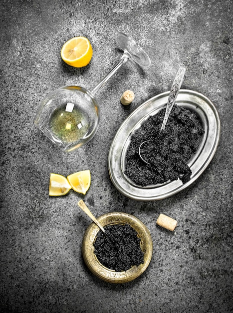 Caviar noir avec un verre de vin blanc. Sur fond rustique.