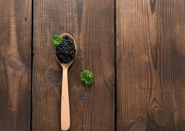 Caviar de paddlefish noir granuleux frais dans une cuillère en bois marron sur fond noir, vue de dessus. Espace de copie