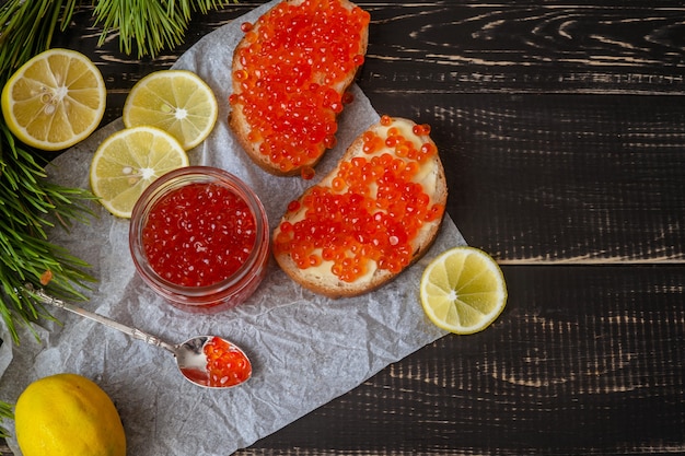 Caviar rouge dans un bocal et sandwichs sur fond de bois noir