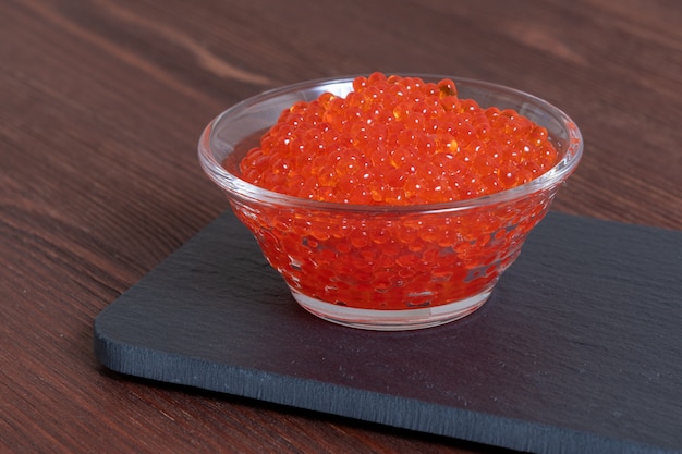 Caviar rouge dans le bocal en verre sur la table en bois brun foncé