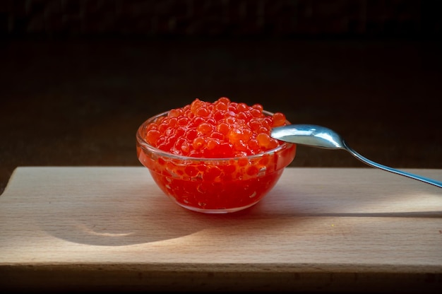 Caviar rouge dans un bol en verre et une cuillère sur un plateau en bois