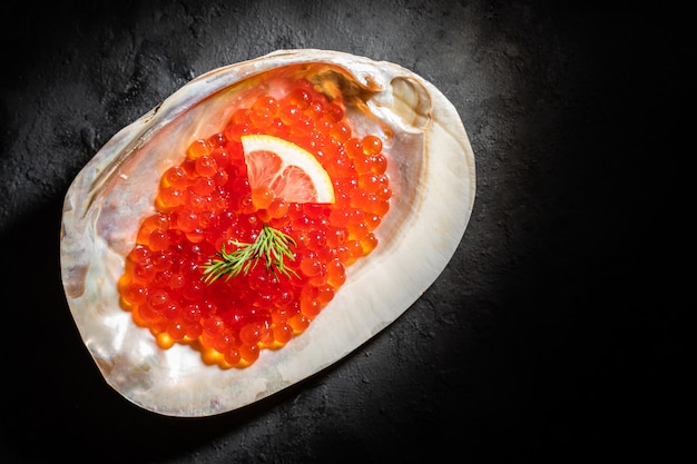 Caviar rouge dans la coquille de mer sur tableau noir.