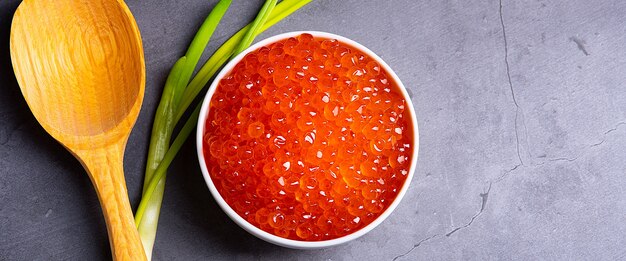 caviar rouge dans une tasse en bois sur fond gris avec une cuillère et des oignons verts un caviar à gros tas