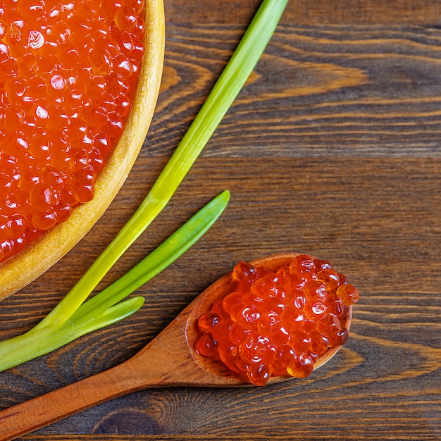 Caviar rouge dans une tasse en bois sur un mur en bois avec une cuillère.