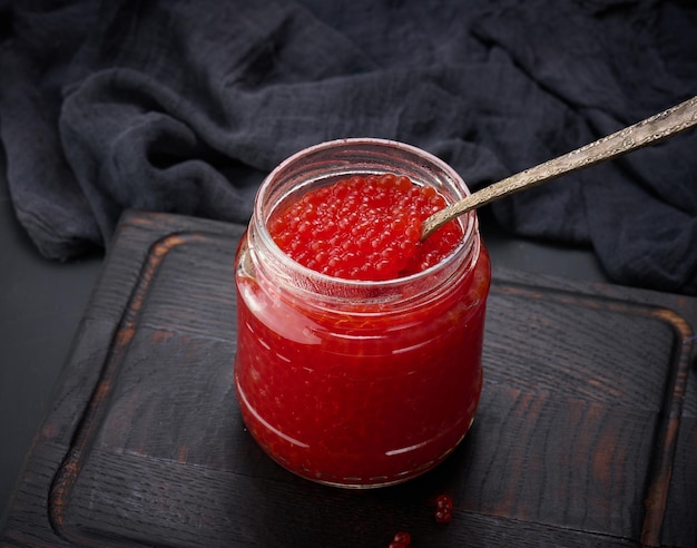 Caviar rouge granuleux frais dans un bocal en verre sur une table en bois