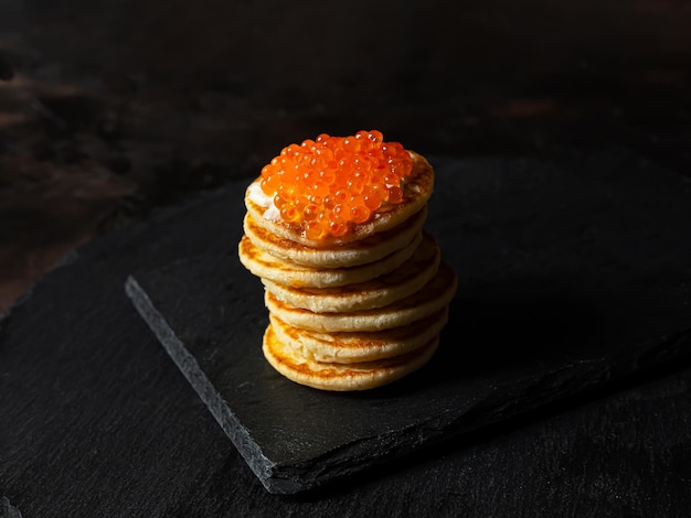 Caviar rouge sur une pile de crêpes à la crème sure sur une ardoise