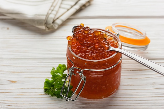 Caviar rouge en pot avec cuillère Fruits de mer avec persil sur table en bois blanc Délicatesse de saumon de luxe Vue latérale