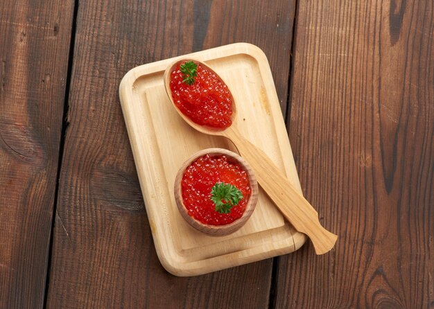 Le caviar rouge de saumon rose se trouve dans une cuillère en bois sur une planche à découper. Table en bois marron, vue de dessus