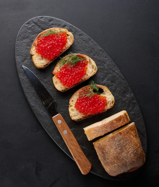 Caviar rouge sur des tranches de pain de blé blanc sur une table noire concept de cuisine de luxe et gourmet