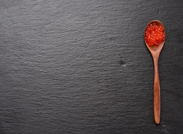 Caviar de saumon kéta rouge à grains frais dans une cuillère en bois, fond noir, espace copie