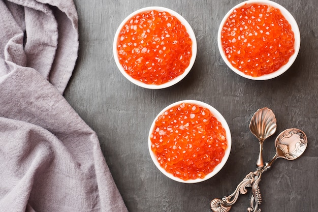 Caviar de saumon rouge dans une assiette sur une table sombre.