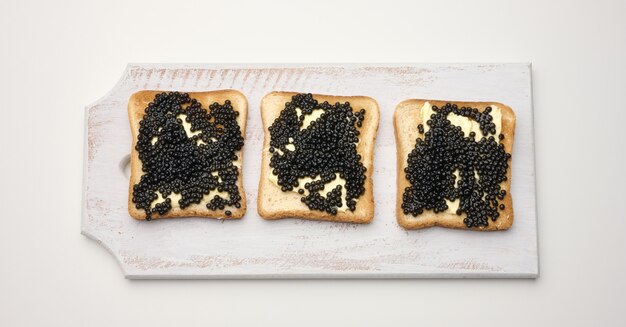 Caviar de spatule sur une tranche carrée de pain de farine de blé blanc sur une planche à découper en bois. Vue de dessus sur tableau blanc