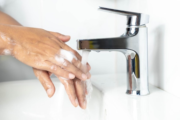 Ceci est une photo d'une main de femme se lavant les mains avec du savon moussant blanc sur un lavabo blanc dans la salle de bain