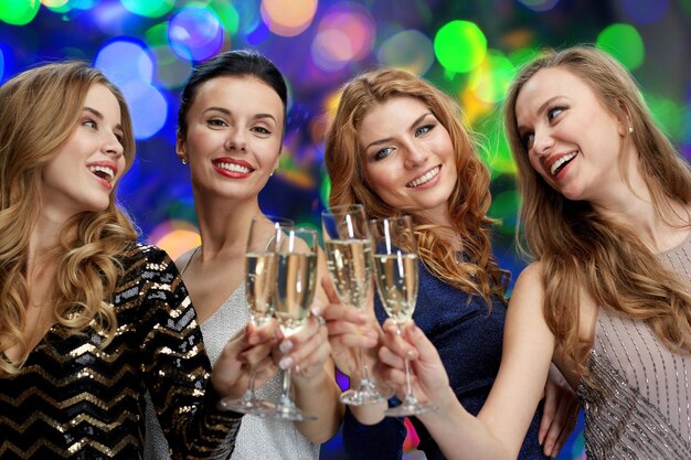 célébration, amis, enterrement de vie de jeune fille et concept de vacances - femmes heureuses faisant tinter des verres de champagne sur fond de lumières