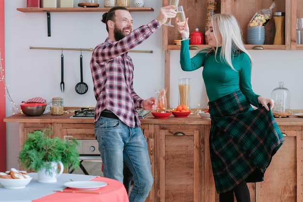 Célébration amusante. Heureux couple tintant des verres de champagne dans une cuisine moderne.